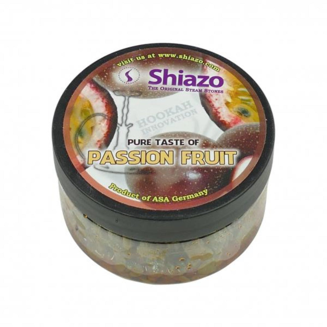 Shiazo Höyrykivet Passion Fruit 100g -pakkaus avattuna, sisältäen höyrykiviä ja taustalla höyryävä vesipiippu trooppisessa ympäristössä.